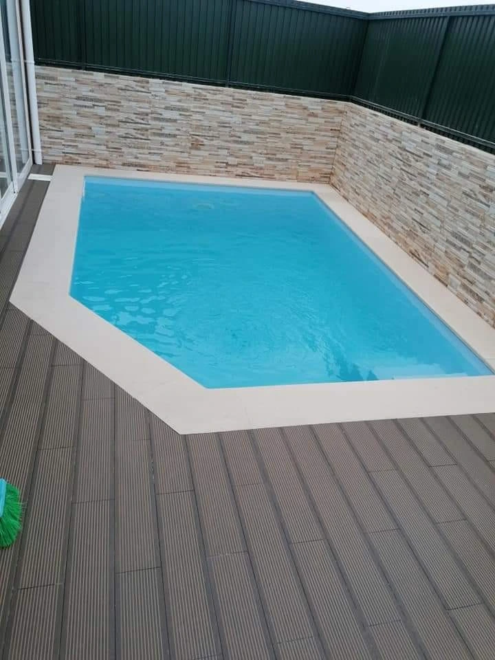 Piscina azul com bordo em pedra e pavimento em deck