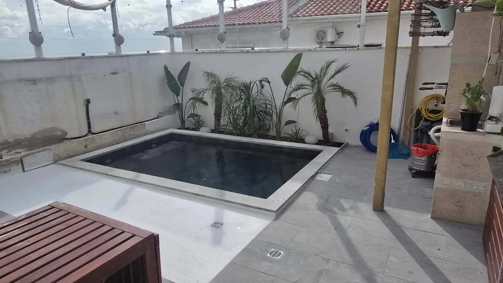 Piscina pronta com revestimento escuro, palmeiras e pavimento em granito